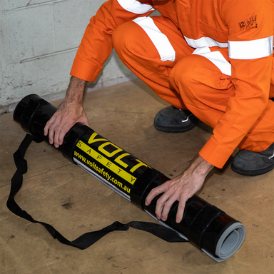 Person in orange safety jumpsuit handling a Volt Safety insulation mat on a concrete floor.